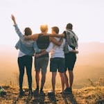 A group of friends embrace while enjoying a sunset view from the mountain top.